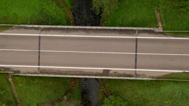 Yeşilliklerle çevrili küçük bir derenin üzerindeki yol köprüsünün havadan görünüşü.