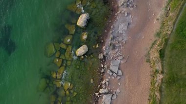 Yeşil suyu ve kumlu plajı olan kayalık bir sahil manzarası..