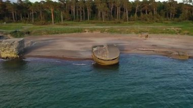 Sahilde ağaçlar ve kayalık bir kıyı şeridi ile çevrili büyük terk edilmiş beton bir savunma yapısı olan bir kıyı bölgesinin havadan görüntüsü..