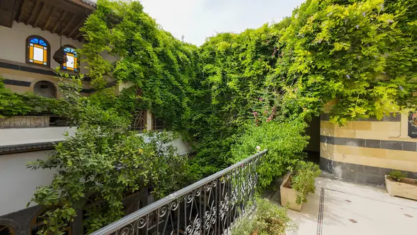 Bol yeşillik, duvarları kaplayan bir avlu ve süslü korkulukları olan bir balkon. Şam 'ın eski kasabasında
