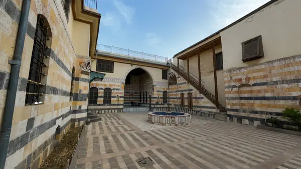 Çizgili taş duvarları, kemerli girişi ve merkezi bir çeşmesi olan tarihi bir avlu. Şam 'ın eski kasabasında