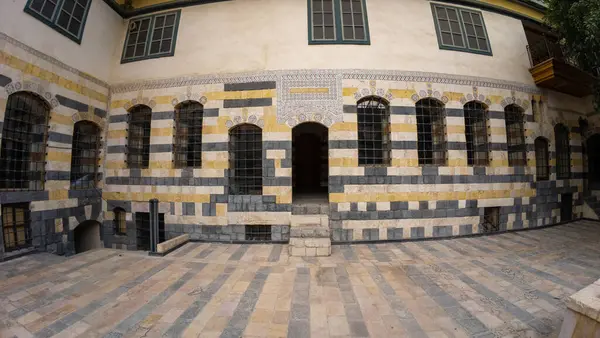 Çizgili taş desenli, kemerli pencereli ve fayanslı avlusu olan tarihi bina cephesi. Şam 'ın eski kasabasında