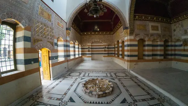 Karmaşık mozaik döşemeleri, çizgili duvarları ve süslü tavanı olan güzel dekore edilmiş bir tarihi oda. Odada kemerli pencereler ve merkezi bir çeşme yer alıyor. Şam 'ın eski kasabasında