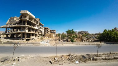 Temiz mavi bir gökyüzü altında yıkılmış binalar ve enkazlarla harap olmuş bir şehir manzarası. Suriye 'nin Şam Jobar ilçesinde