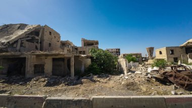 Temiz mavi bir gökyüzü altında harap olmuş binalar ve enkazlarla ıssız bir şehir manzarası. Suriye 'nin Şam Jobar ilçesinde