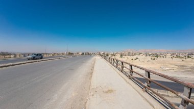 Temiz mavi gökyüzünün altında, çorak arazinin ve uzak binaların kuşattığı, tek arabalı geniş bir yol. Suriye 'nin Şam Jobar ilçesinde