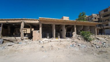Açık mavi gökyüzünün altında enkaz ve molozlarla çevrili, gözle görülür yapısal hasarı olan harap bir bina. Suriye 'nin Şam Jobar ilçesinde