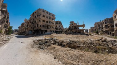 Açık mavi gökyüzü altında terk edilmiş, hasarlı binaların olduğu, savaştan zarar görmüş kentsel bir bölgenin panoramik görüntüsü. Suriye 'nin Şam Jobar ilçesinde