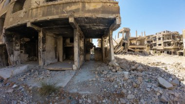 Temiz mavi bir gökyüzünün altında yıkılmış binalar ve molozlarla harap olmuş bir şehir manzarası. Suriye 'nin Şam Jobar ilçesinde