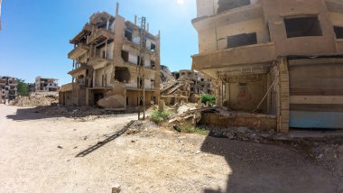 Temiz mavi bir gökyüzü altında hasarlı binalar ve enkazlar olan savaştan zarar görmüş bir şehir manzarası. Suriye 'nin Şam Jobar ilçesinde