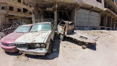 Terk edilmiş, paslı arabalar harap olmuş bir binanın önünde, şehir çürümesi. Suriye 'nin Şam Jobar ilçesinde