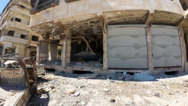 Kısmen çökmüş ön cephesi ve enkazı etrafa saçılmış hasarlı bir bina. Terk edilmiş bir araba binanın içinde görünüyor ve bölge terk edilmiş ve terk edilmiş görünüyor..