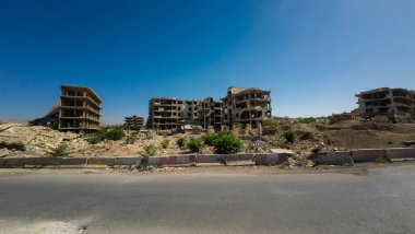 Terk edilmiş, kısmen yıkılmış binalar açık mavi gökyüzünün altındaki ıssız bir alanda. Suriye 'nin Şam Jobar ilçesinde