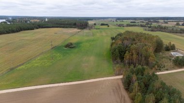 Bulutlu bir gökyüzünün altında tarlaları, ağaçları ve elektrik hatları olan kırsal bir arazinin havadan görünüşü.
