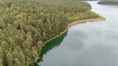 Durgun bir ormanın göl kıyısının gökyüzünü yansıtan sakin sularının havadan görünüşü..