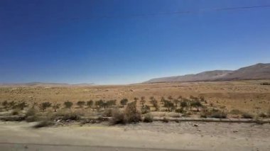 Uçsuz bucaksız bir çöl manzarası berrak mavi bir gökyüzü ve hareket halindeki bir arabadan uzak dağlar. Suriye 'de.