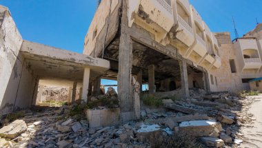 Açık mavi bir gökyüzünün altında, beton ve enkazla meydana gelen bir terörist saldırısı sonucu kısmen çökmüş bir bina..