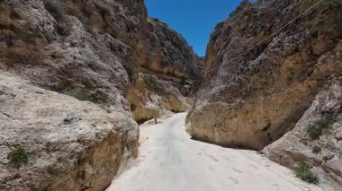 Dar, sarp, engebeli duvarları açık mavi gökyüzünün altında kayalık bir kanyon..