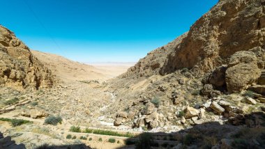 Uçsuz bucaksız, kayalık bir çöl manzarası engebeli uçurumlar ve berrak mavi bir gökyüzü.