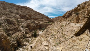 Kayalık tepeleri ve açık mavi gökyüzü olan engebeli bir çöl manzarası..