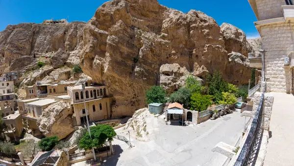 Büyük bir uçuruma kurulmuş antik taş binaların yer aldığı kayalık bir arazinin panoramik görüntüsü. Sahne, açık mavi gökyüzü ile güneşli bir günü yakalıyor, doğal güzelliği gözler önüne seriyor..