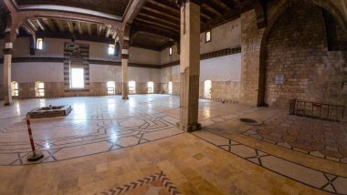 Geniş, boş, karmaşık zemin desenleri, taş duvarları ve ahşap tavan kirişleri olan bir tarih salonu. Odada kemerli pencereler var. Antik Halep şehri kale taht odası, Suriye