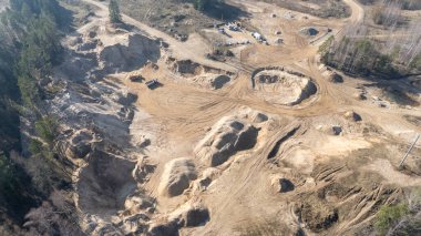 Kazı alanları ve toprak yolları olan, seyrek ağaçlarla çevrili bir kum ocağının havadan görünüşü..