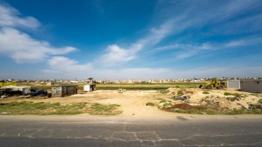 İnşaat ekipmanlarıyla ve mavi gökyüzünün altındaki uzak binalarla dolu bir kırsal alan. Kırsal Suriye