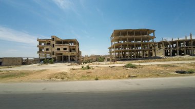 Terk edilmiş, tamamlanmamış binalar, açık mavi gökyüzünün altındaki ıssız bir alanda. Kırsal Suriye