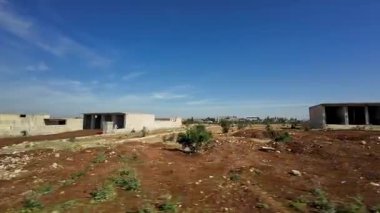 Dağınık evlerle, toprak yollarla ve açık mavi gökyüzüyle kırsal alan. Kırsal Suriye