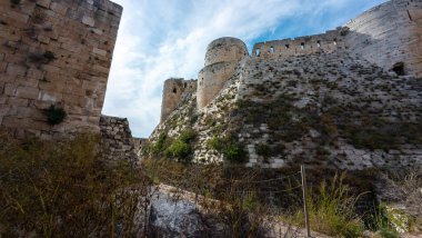 Mavi gökyüzünün altında taş duvarları ve kuleleri olan görkemli bir ortaçağ kalesi. Krak des Chevaliers kalesi, Suriye