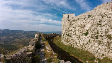 Uçsuz bucaksız manzaralı bir tepedeki antik taş kalenin panoramik görüntüsü. Krak des Chevaliers kalesi, Suriye