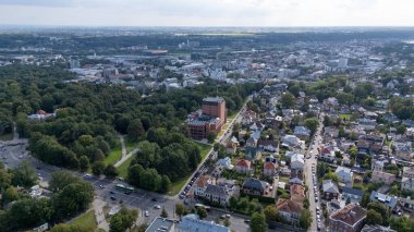 Kentsel ve yeşil alanların karışımından oluşan bir şehir manzarası. Konut binaları, merkez park ve bulutlu bir gökyüzünün altında uzak bir ufuk..