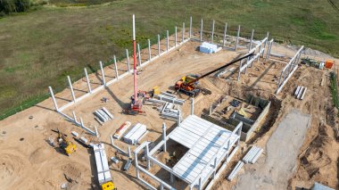 Vinçlerin ve çelik kirişlerin monte edildiği bir inşaat alanının havadan görüntüsü.