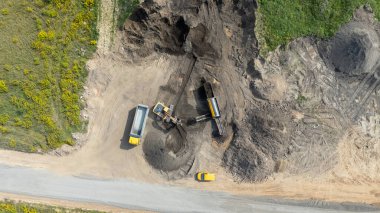Kazı makineleri ve toprak taşıyan çöp kamyonlarıyla inşaat alanının havadan görüntüsü.
