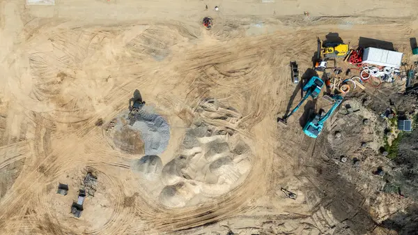 Makine ve kum yığınları olan bir inşaat alanının havadan görüntüsü.