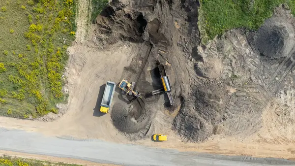 Kazı makineleri ve toprak taşıyan çöp kamyonlarıyla inşaat alanının havadan görüntüsü.