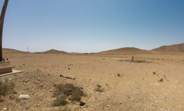 Uçsuz bucaksız çöl manzarası berrak mavi gökyüzü ve uzak tepeler.