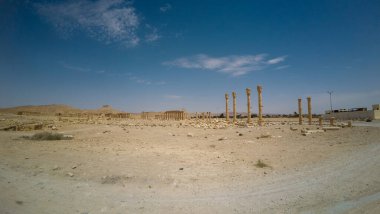 Çölün ortasında berrak mavi bir gökyüzünün altında uzun sütunları olan antik kalıntılar..