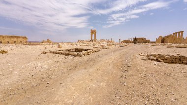 IŞİD tarafından mavi gökyüzünün altında bulutlu bir çöl manzarasında yıkılmış antik kalıntılar. Suriye, Palmira.