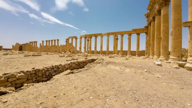 IŞİD tarafından mavi gökyüzünün altında bulutlu bir çöl manzarasında yıkılmış antik kalıntılar. Suriye, Palmira.