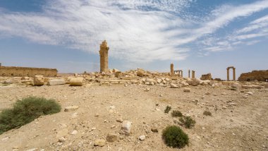 IŞİD tarafından mavi gökyüzünün altında bulutlu bir çöl manzarasında yıkılmış antik kalıntılar. Suriye, Palmira.