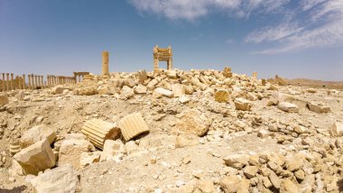 IŞİD tarafından mavi gökyüzünün altında bulutlu bir çöl manzarasında yıkılmış antik kalıntılar. Suriye, Palmira.