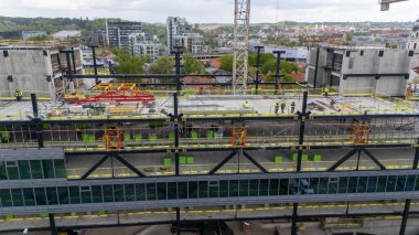 İşçilerin, vinçlerin ve inşaat malzemelerinin bulunduğu bir inşaat alanının havadan görünüşü, modern mimari ve kentsel gelişimi gösteriyor