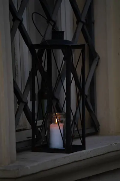 İçinde parlayan bir mum olan siyah metal bir fener pencere pervazında ya da çıkıntıda durur. Alevin sıcacık ışığı çevreyi aydınlatır.