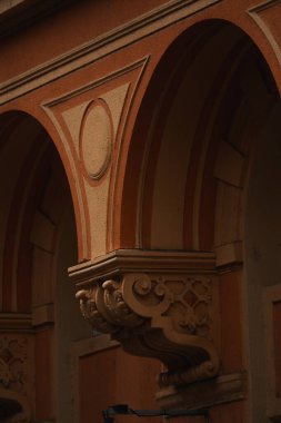 Yakın plan bir binanın dış cephesinin karmaşık mimari detaylarını vurgular, tekrarlayan kemer, sütun ve dekoratif öğelerin yer aldığı bir bölüme odaklanır