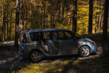 Güneş lekeli bir ormanın içinde, yolcu kapısı biraz aralık olan kirli bir patika. Çam veya ladin gibi etrafındaki ağaçlar, uzun gölgeler oluşturan ve parlak sarı-yeşil yaprakları aydınlatan sıcak, altın güneş ışığıyla aydınlatılıyor. Şey...