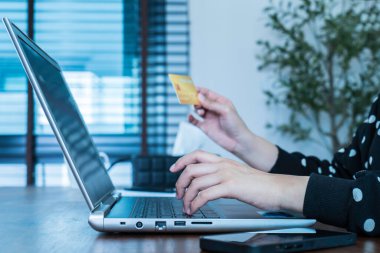 Evde çalışan genç bir kadın dizüstü bilgisayar kullanıyor ve online alışveriş, e-ticaret ve internet bankacılığı için kredi kartı tutuyor. Ödeme metodu ulaşılamaz para. Çevrimiçi alışveriş kavramı.