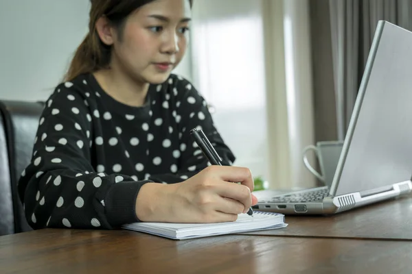 Young asian woman pupil writing notes in notebook at work table, distance learning studying online makes goals checklist at home office. Checklist planning investigate enthusiastic concept.