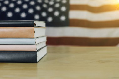 Amerika Birleşik Devletleri bayrağıyla ahşap masanın üzerine yığılmış pek çok kitabın basit bir kompozisyonu. Bir tanesi kopyalama alanı ile açılıyor..